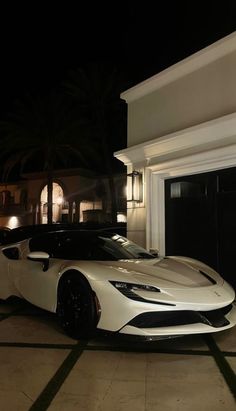 a white sports car is parked in front of a house at night with its lights on