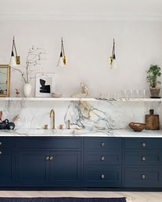 a kitchen with blue cabinets and marble counter tops, gold faucets and hanging lights