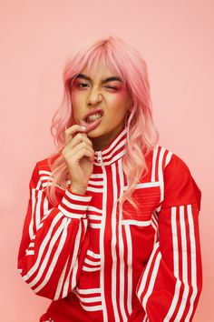 a woman with pink hair wearing a red and white striped shirt posing for the camera