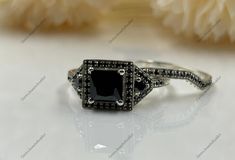 a black and white diamond ring on a table with flowers in the background stock photo