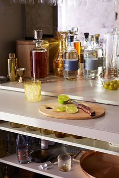 bottles and glasses are sitting on the counter next to a cutting board with limes