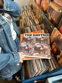 a person holding up a record album in front of a pile of records on the floor