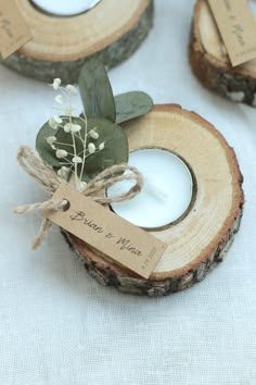 two wooden slices with small white candles in them and some tags attached to the wood