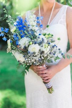 a woman in a white dress holding a bouquet of blue and white flowers on her wedding day