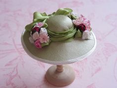 a green hat with pink flowers on it sitting on top of a white tablecloth