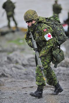 a man in camouflage carrying a medical pack and walking with other soldiers on the ground behind him