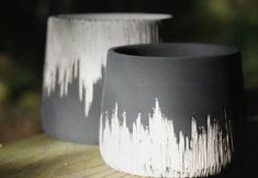 two black and white vases sitting on top of a wooden table next to each other