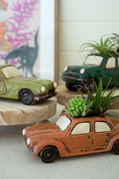 two toy cars with succulents in them on a table next to another car