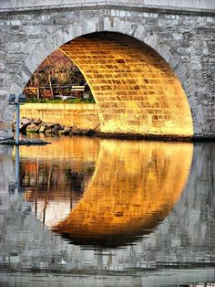 an arched stone bridge over a body of water with trees in the background and reflections on the water