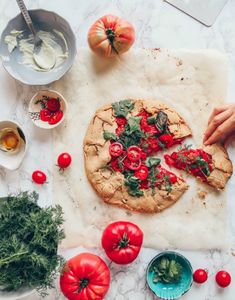 a pizza sitting on top of a white counter next to tomatoes and other food items