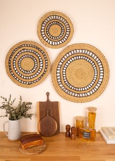 three woven wall hangings on the wall above a wooden cutting board and potted plant