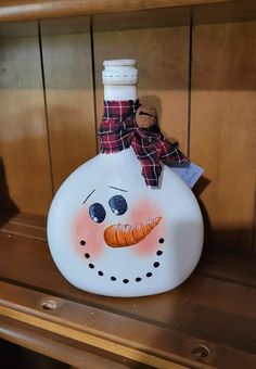 a painted snowman bottle sitting on top of a wooden shelf next to a wood paneled wall