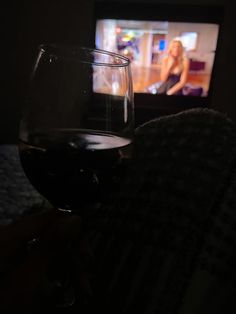 a person holding a glass of wine in front of a television