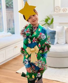 a young boy wearing a green christmas sweater with a yellow star on his head, standing in a living room