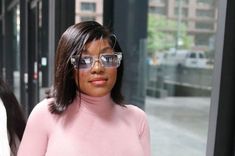 a woman in pink sweater and sunglasses walking down the street with other people behind her