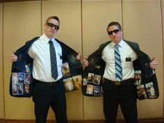 two men standing next to each other in front of a wall with pictures on it