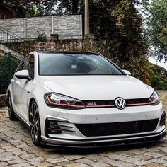 a white volkswagen car parked in front of a stone wall with stairs leading up to it