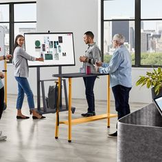 four people standing around a table with a white board on it in an office setting