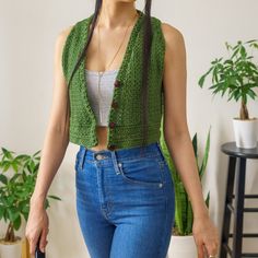 a woman in jeans and a tank top is holding a handbag while standing next to a potted plant