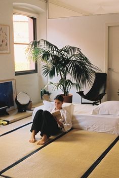 a man sitting on top of a bed next to a plant in a living room