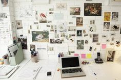 a white desk topped with a laptop computer and lots of pictures on the wall behind it