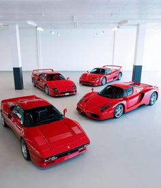 four red sports cars are parked in an empty room with white walls and flooring