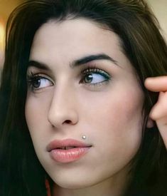 a close up of a woman with blue eyes and piercings on her nose looking at the camera