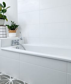 a white bath tub sitting next to a plant on top of a tiled floor in a bathroom