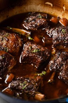 a pot full of stew with meat and carrots on the side, ready to be eaten