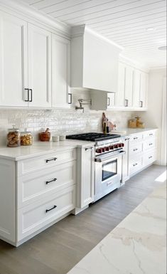 a kitchen with white cabinets and marble counter tops, along with an oven in the center