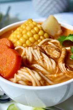 a white bowl filled with noodles, carrots and corn on top of a table