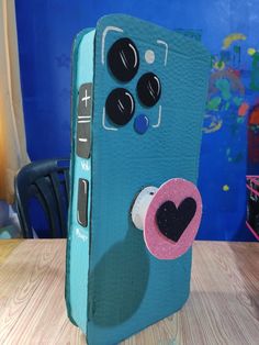 a cell phone case with a heart on the side and buttons attached to it, sitting on a table