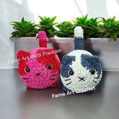 two crocheted cats sitting next to each other on top of a table in front of a potted plant