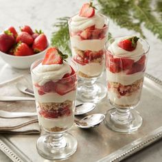 three desserts with strawberries and whipped cream in them on a silver serving tray