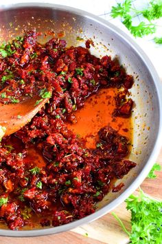 a pan filled with sauce and vegetables on top of a wooden cutting board next to parsley