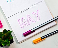 a notepad with the word may written on it next to some pens and a plant