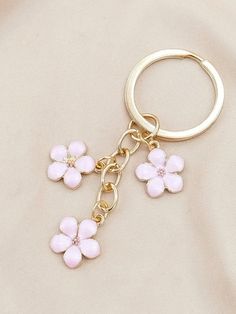 a gold key chain with pink flowers hanging from it's center and two smaller white flowers on each side