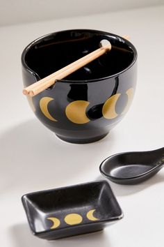 a black bowl with yellow circles and two spoons next to it on a white surface