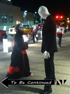 a man and woman dressed up in costumes standing on the street at night with traffic lights behind them