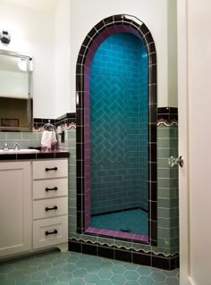 a bathroom with blue and black tiles on the shower wall, sink and vanity area