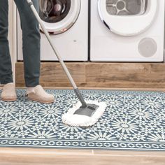 a person using a mop to clean the floor in front of washer and dryer