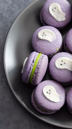 purple macaroons decorated with white icing and ghost eyes on a gray plate