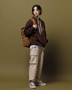 a young man standing in front of a brown wall wearing a brown sweatshirt and khaki pants