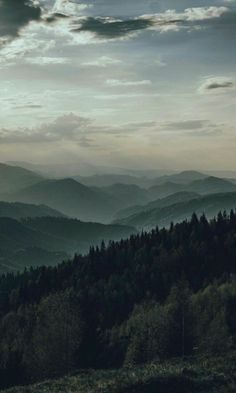 the mountains are covered with trees and clouds in the distance, under a cloudy sky