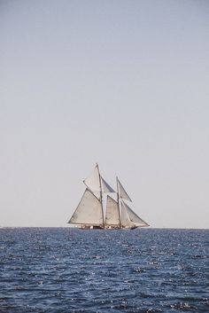 an old fashioned sailboat in the middle of the ocean on a clear, blue day