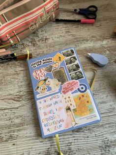 an open notebook sitting on top of a wooden table next to scissors and other items