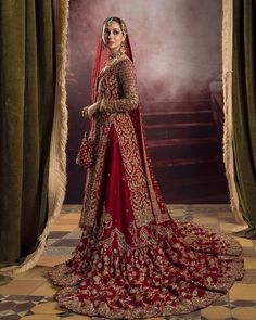 a woman in a red and gold bridal gown posing for the camera with her hands on her hips