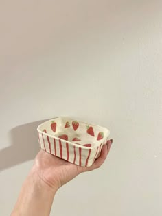 a hand holding a small bowl with strawberries on the inside and stripes around it