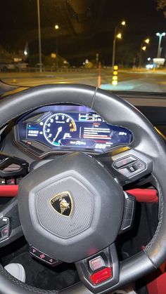 the steering wheel and dashboard of a sports car in a parking lot at night time