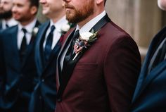 a group of men in suits and ties standing next to each other with one man wearing a boutonniere